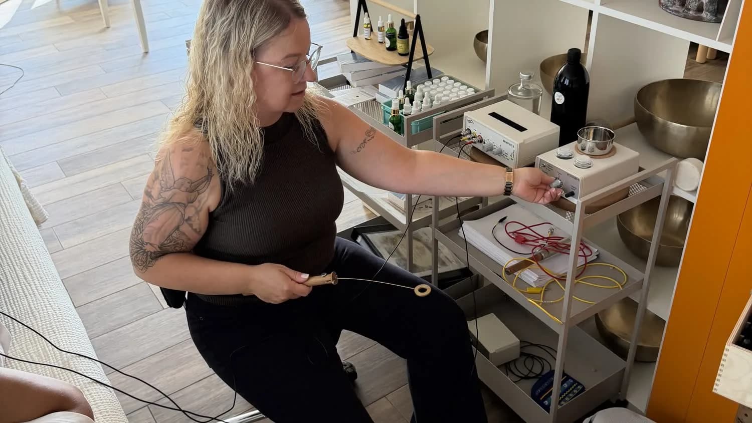 Mariana sitzt neben ihrem Arbeitswagen mit Klangschalen und kleinen Fläschchen und hält einen Griff in der Hand.