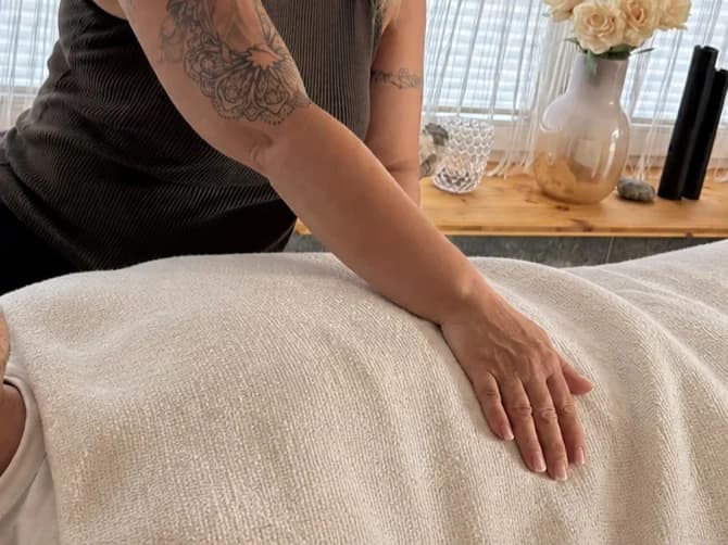Mariana legt einer angezogen und zugedeckt ruhenden Person eine Hand auf.