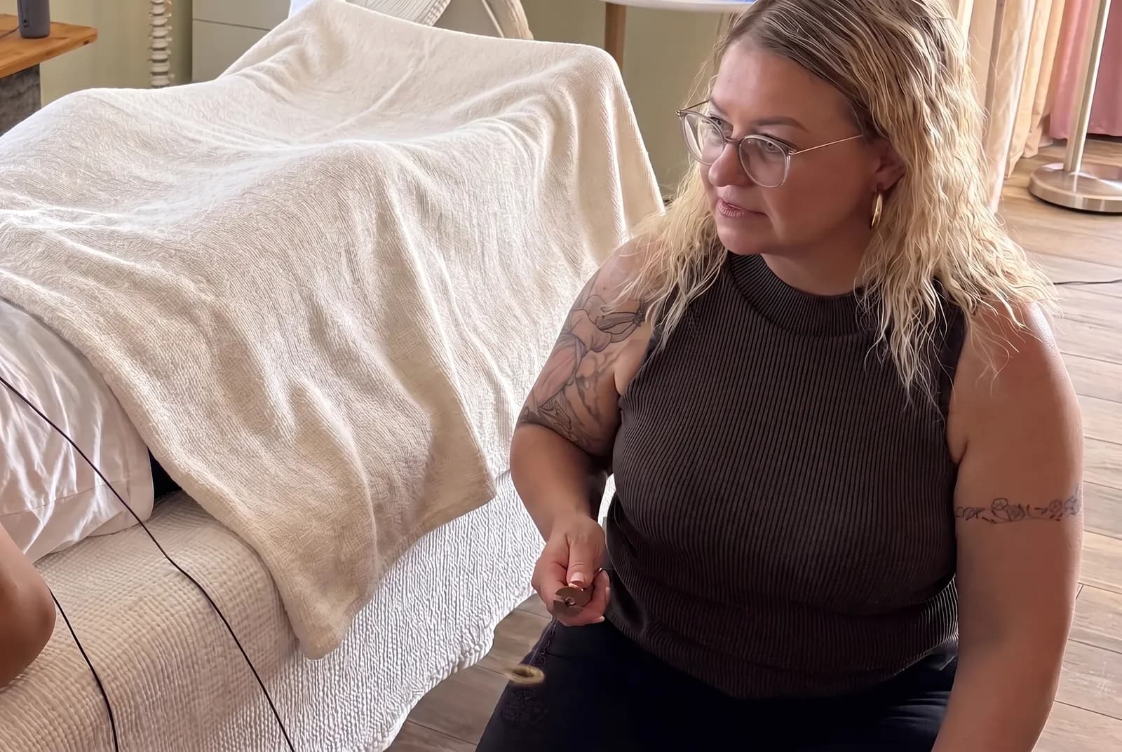 Mariana sitzt auf einem Hocker neben der Liege, auf der eine Person angezogen und zugedeckt ruht.