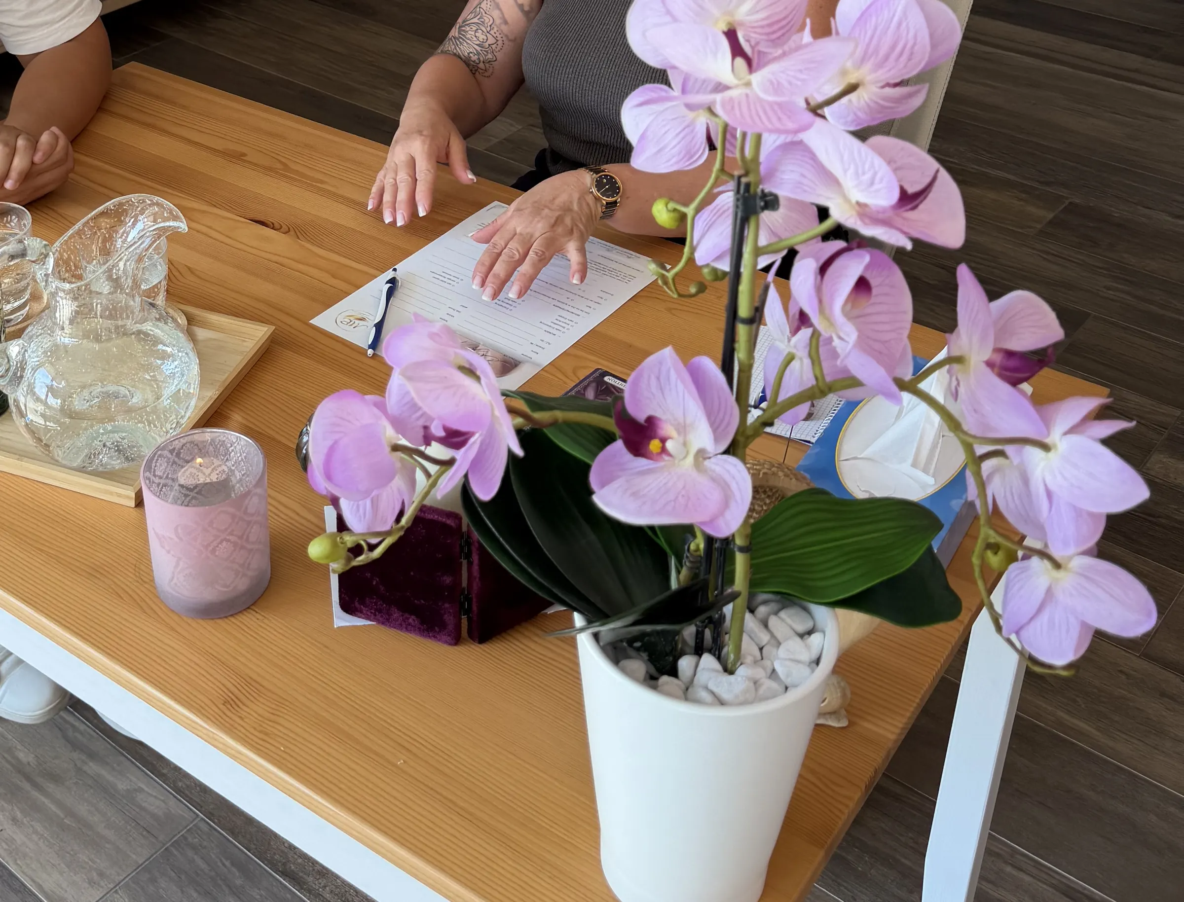 Eine Orchidee steht auf dem Gesprächstisch, daneben ein Wasserkrug, ein Windlicht und Notizen.